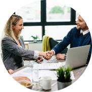 Business professionals shaking hands during an initial consultation, sitting at a desk with a laptop and documents