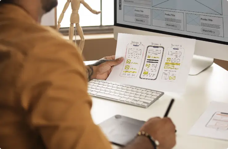 Developer reviewing mobile app wireframes and designs at a desk with a computer, representing comprehensive mobile app development services