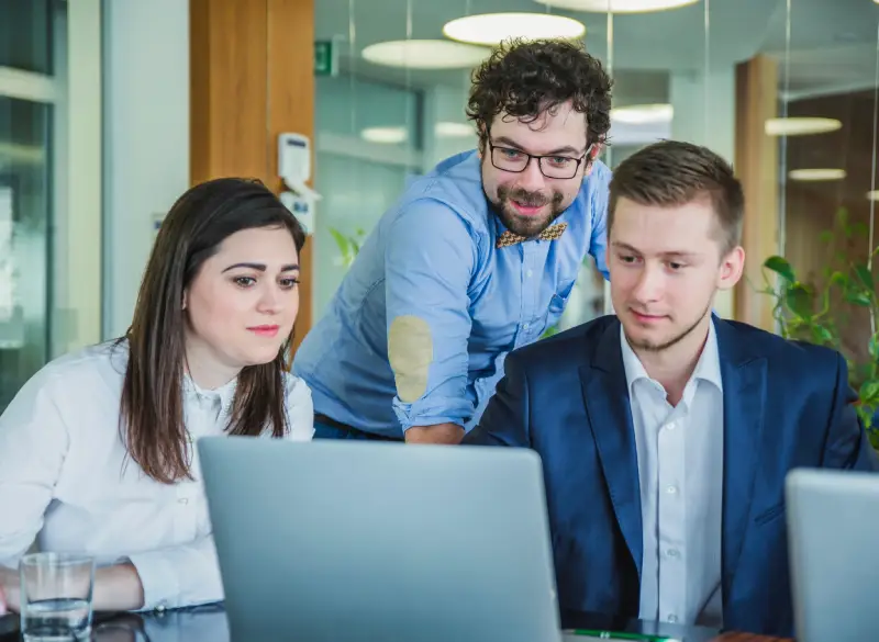 A diverse team of professionals collaborating on a laptop, representing the customized strategies and personalized client focus of Techpullers' social media marketing services.