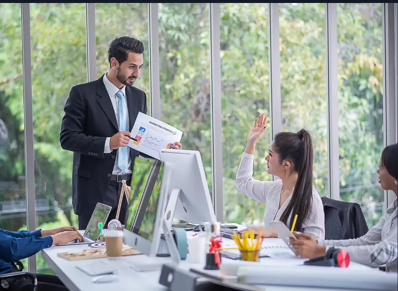 A team of marketing professionals collaborating in a modern office, with a man in a suit presenting a marketing report to colleagues, showcasing the seasoned expertise of Techpullers' social media marketing team.