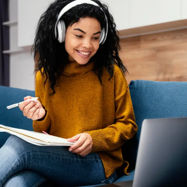 Woman with headphones studying and smiling, representing TechPullers' design of an educational platform for IBS, offering comprehensive learning programs for bankers.